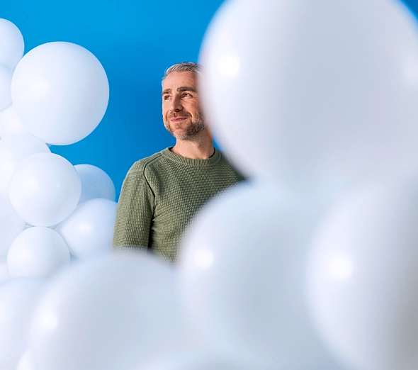 Ein Mann schaut freundlich aus Wolken aus Luftballons heraus